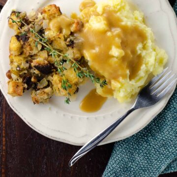 the best vegetarian gravy poured over mashed potatoes and stuffing on a plate with a fork and cloth napkin