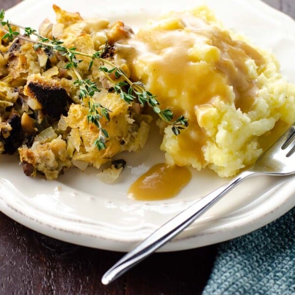 the best vegetarian gravy poured over mashed potatoes and stuffing on a plate with a fork and cloth napkin