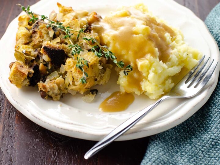 the best vegetarian gravy poured over mashed potatoes and stuffing on a plate with a fork and cloth napkin