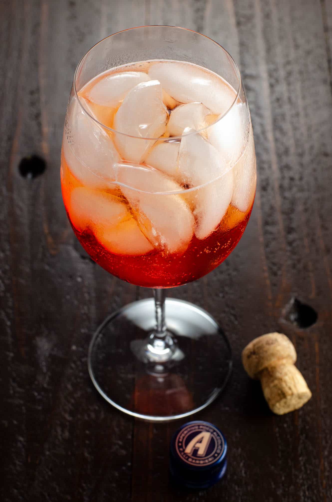 an aperol spritz (3 2 1 recipe) in a large wine glass on a wooden table with a cork