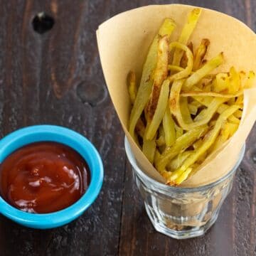 crispy oven baked yukon gold french fries in a paper cone with ketchup