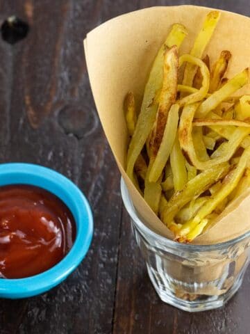 crispy oven baked yukon gold french fries in a paper cone with ketchup