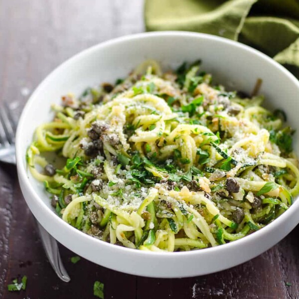 zoodles recipe with lemon caper butter in a white bowl with a fork and green napkin