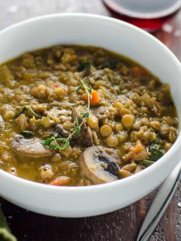 mushroom lentil stew with spinach in a bowl with a spoon and a glass of red wine