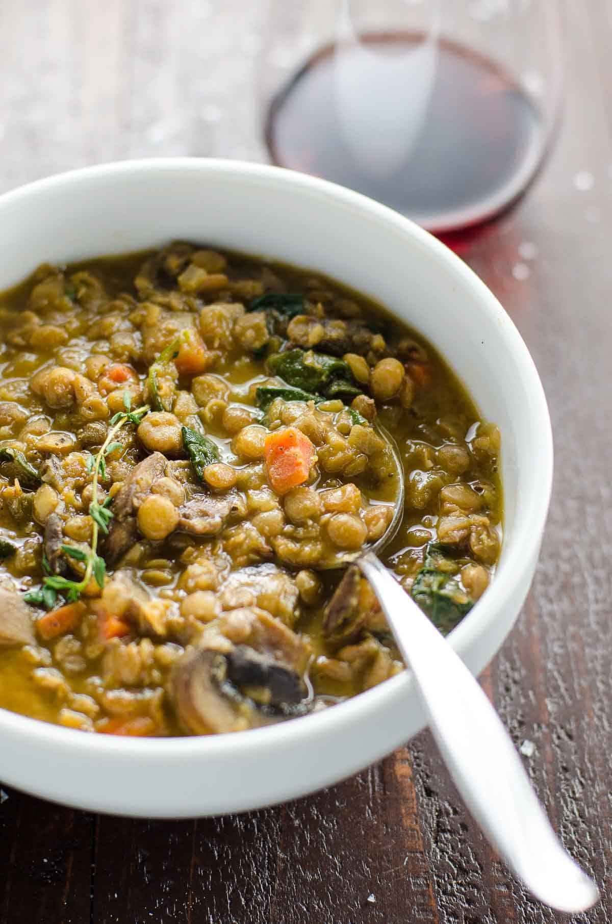 mushroom lentil stew with spinach in a bowl with a spoon and a glass of red wine