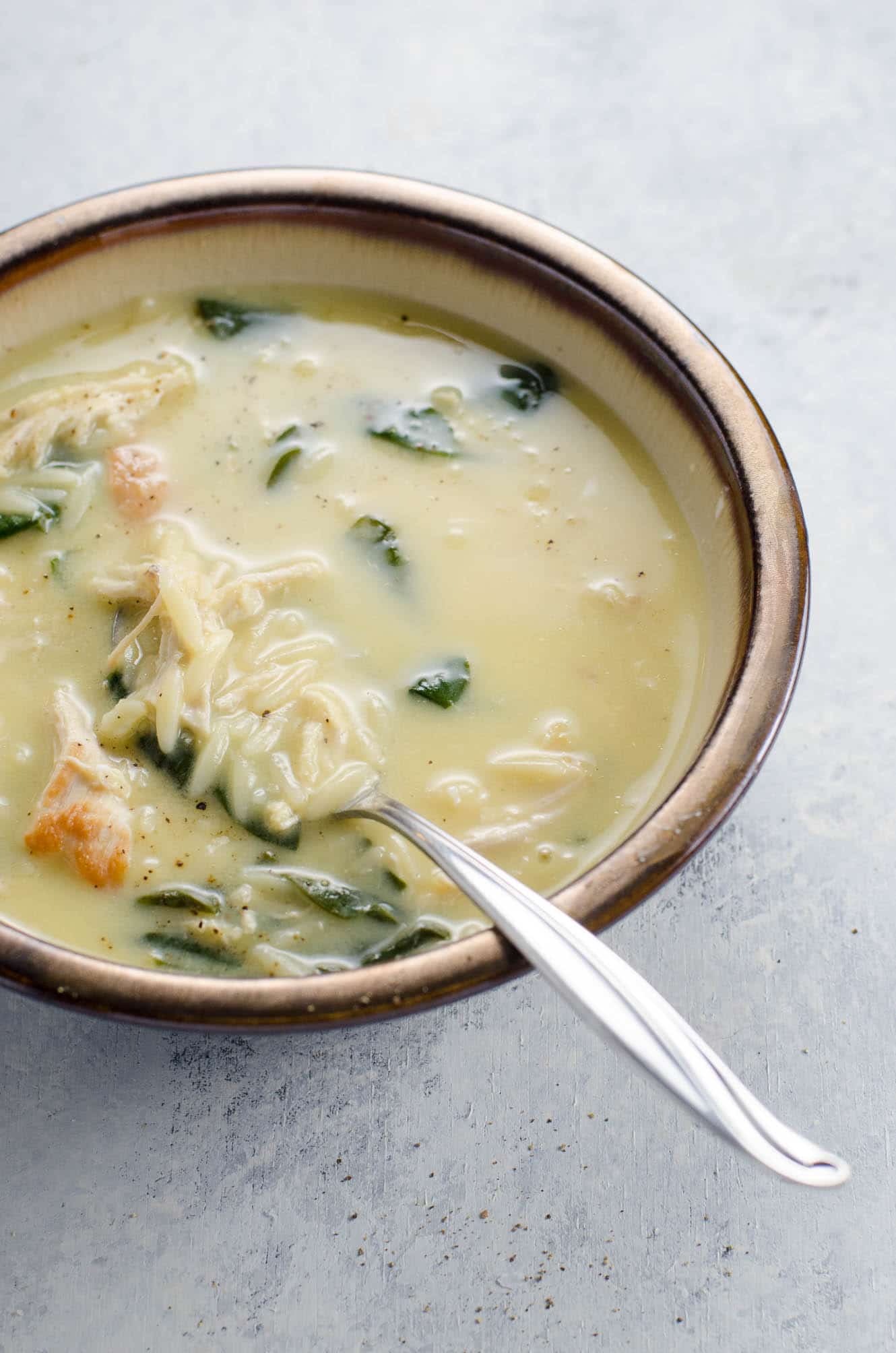 avgolemono soup with orzo (greek lemon chicken soup with orzo) and spinach in a bowl with a spoon