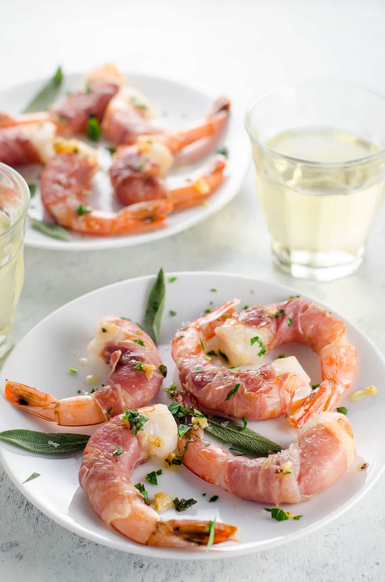 prosciutto wrapped shrimp on small plates with a glass of white wine