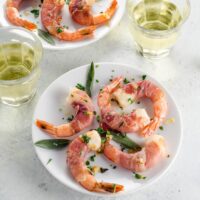 prosciutto wrapped shrimp on small plates with white wine