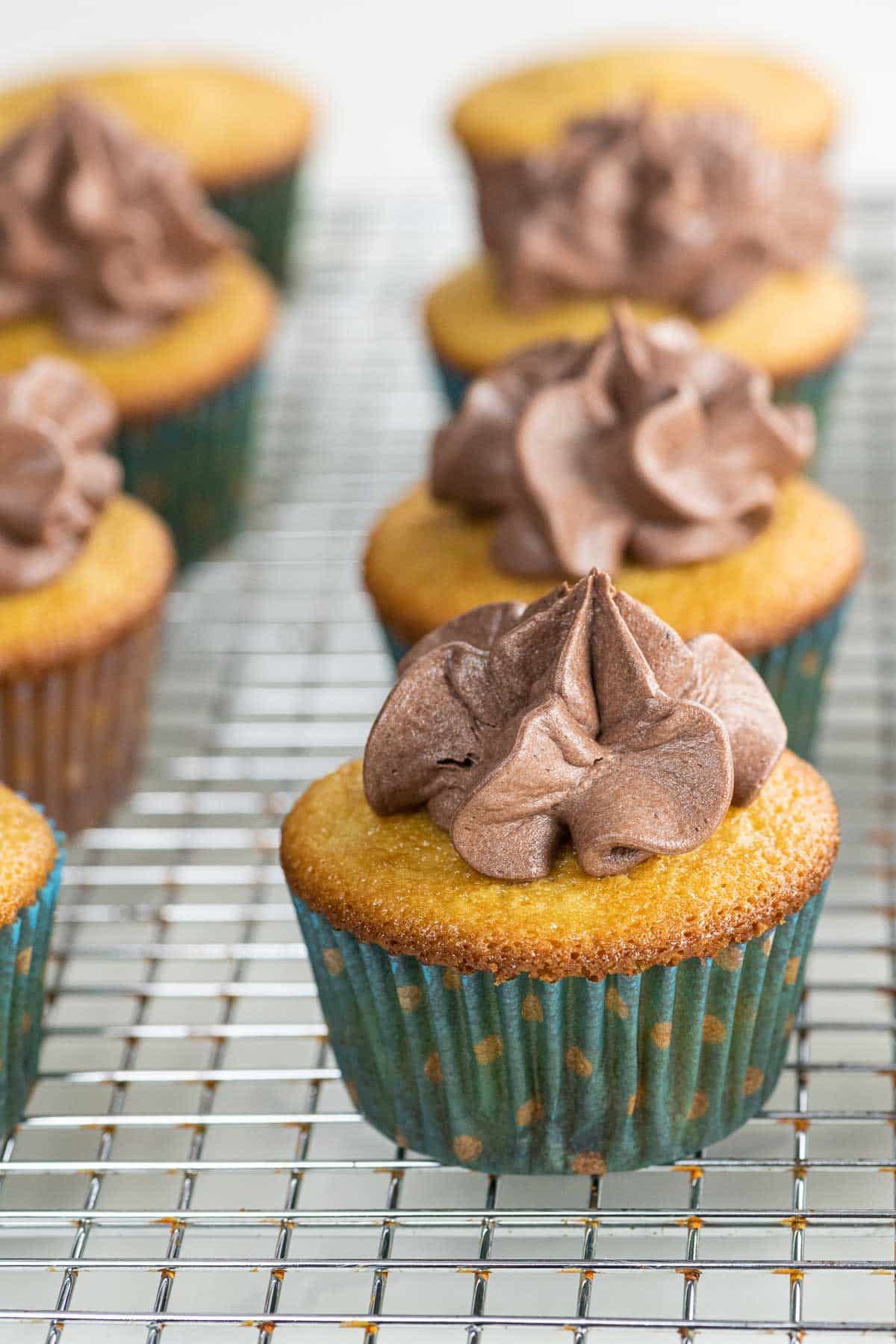 ultimate vanilla cupcakes with whipped chocolate frosting on a cooling rack