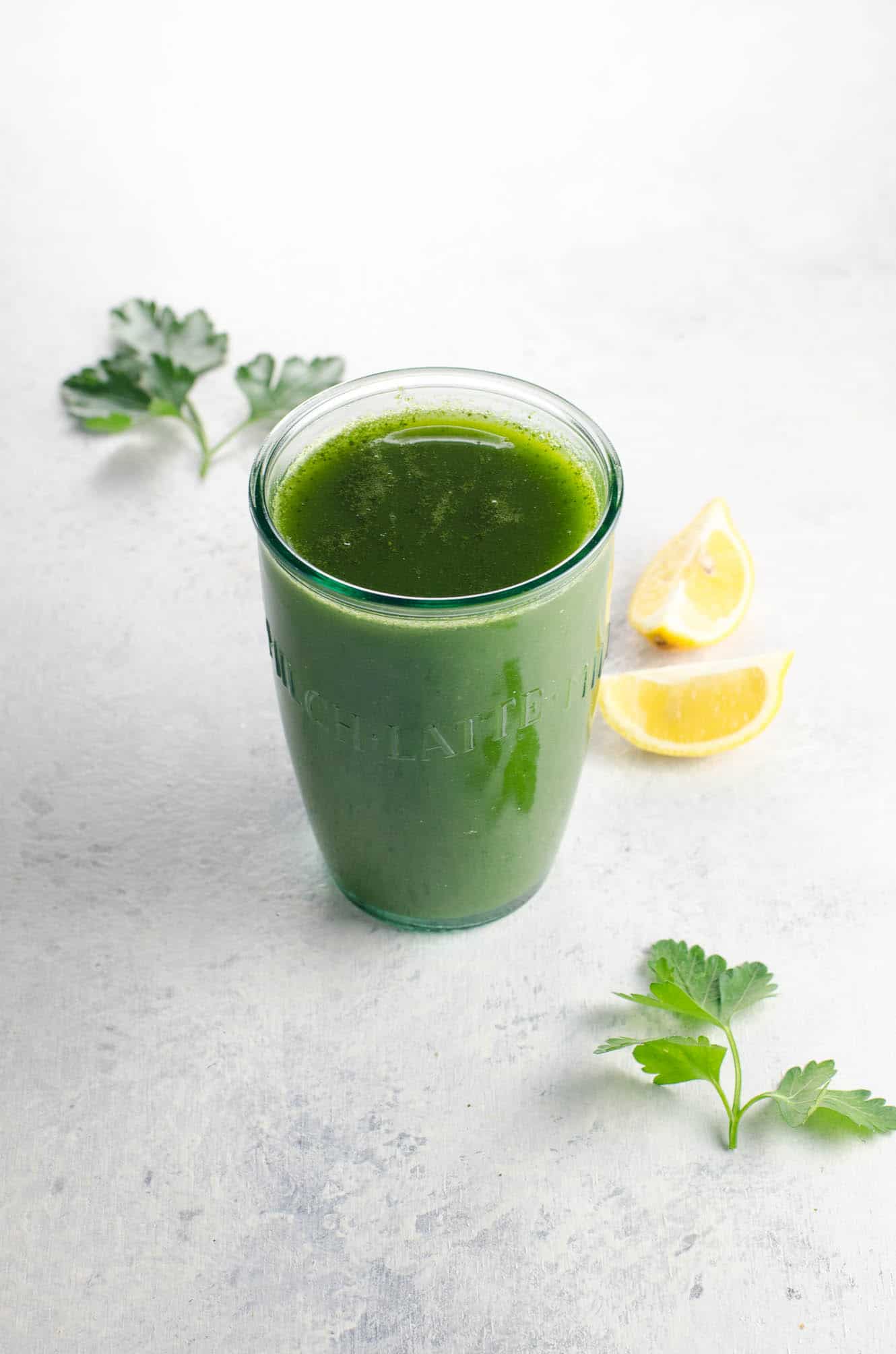 a lovable green juice for weight loss in a glass with parsley and lemon wedges