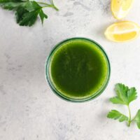 a lovable green juice for weight loss in a glass with parsley and lemon wedges