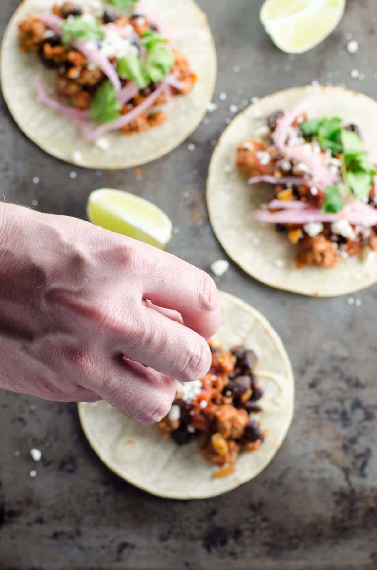 a hand garnishing a ground pork taco