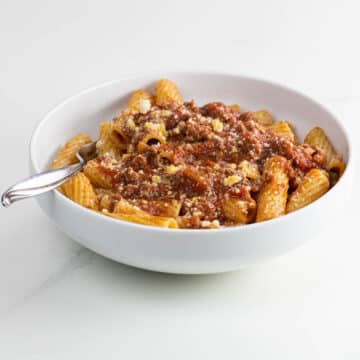 rigatoni bolognese in a white bowl with a fork
