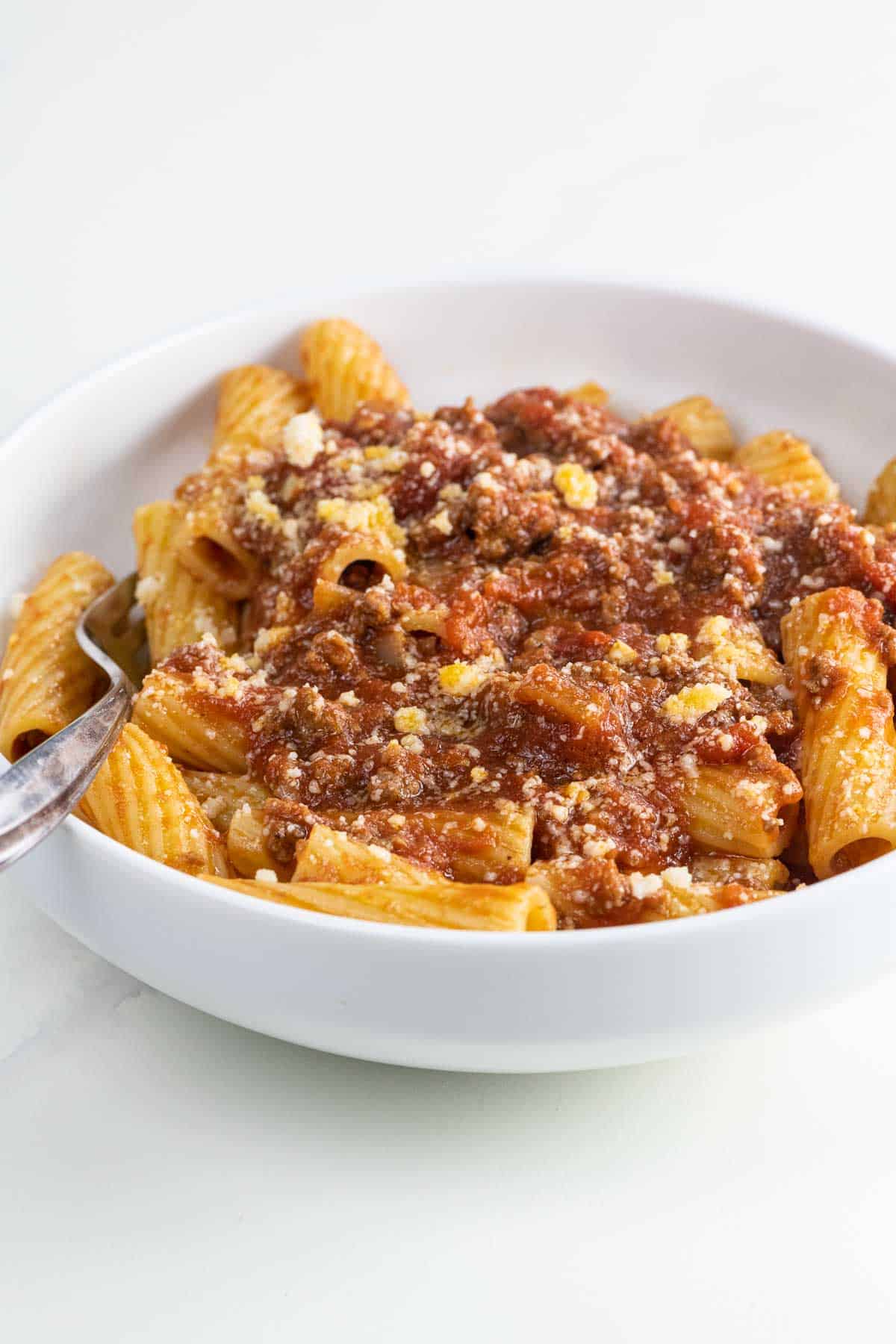 rigatoni bolognese in a white bowl with a fork