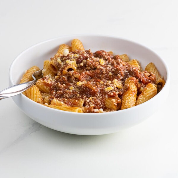rigatoni bolognese in a white bowl with a fork
