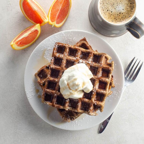 gingerbread waffles topped with whipped cream and syrup with orange wedges and coffee