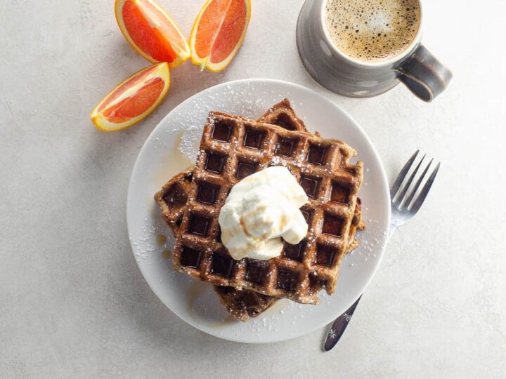 gingerbread waffles topped with whipped cream and syrup with orange wedges and coffee