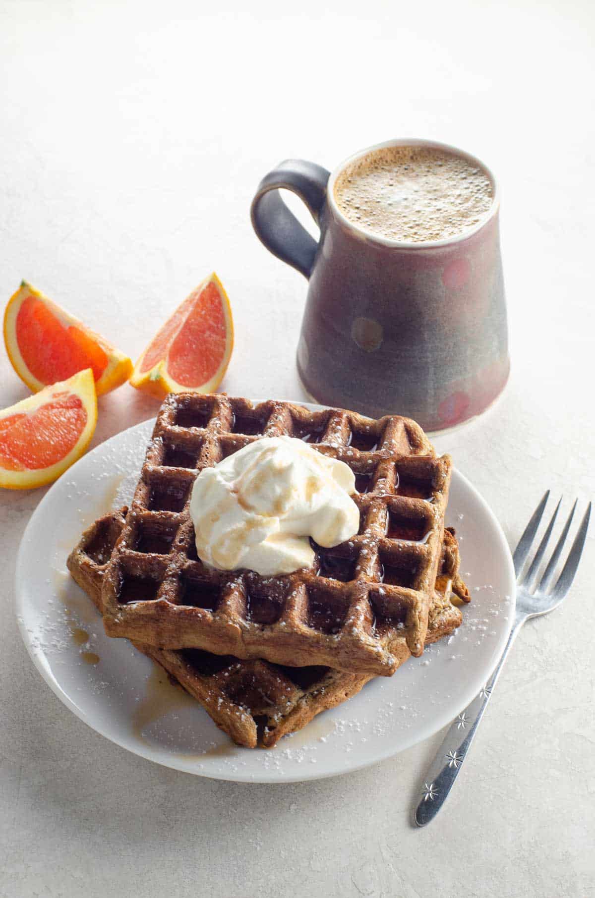 gingerbread waffles topped with whipped cream and syrup with orange wedges and coffee