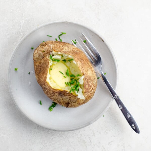 a baked potato with butter and chives on a plate with a fork