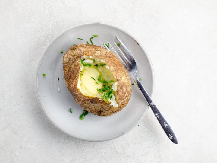 a baked potato with butter and chives on a plate with a fork