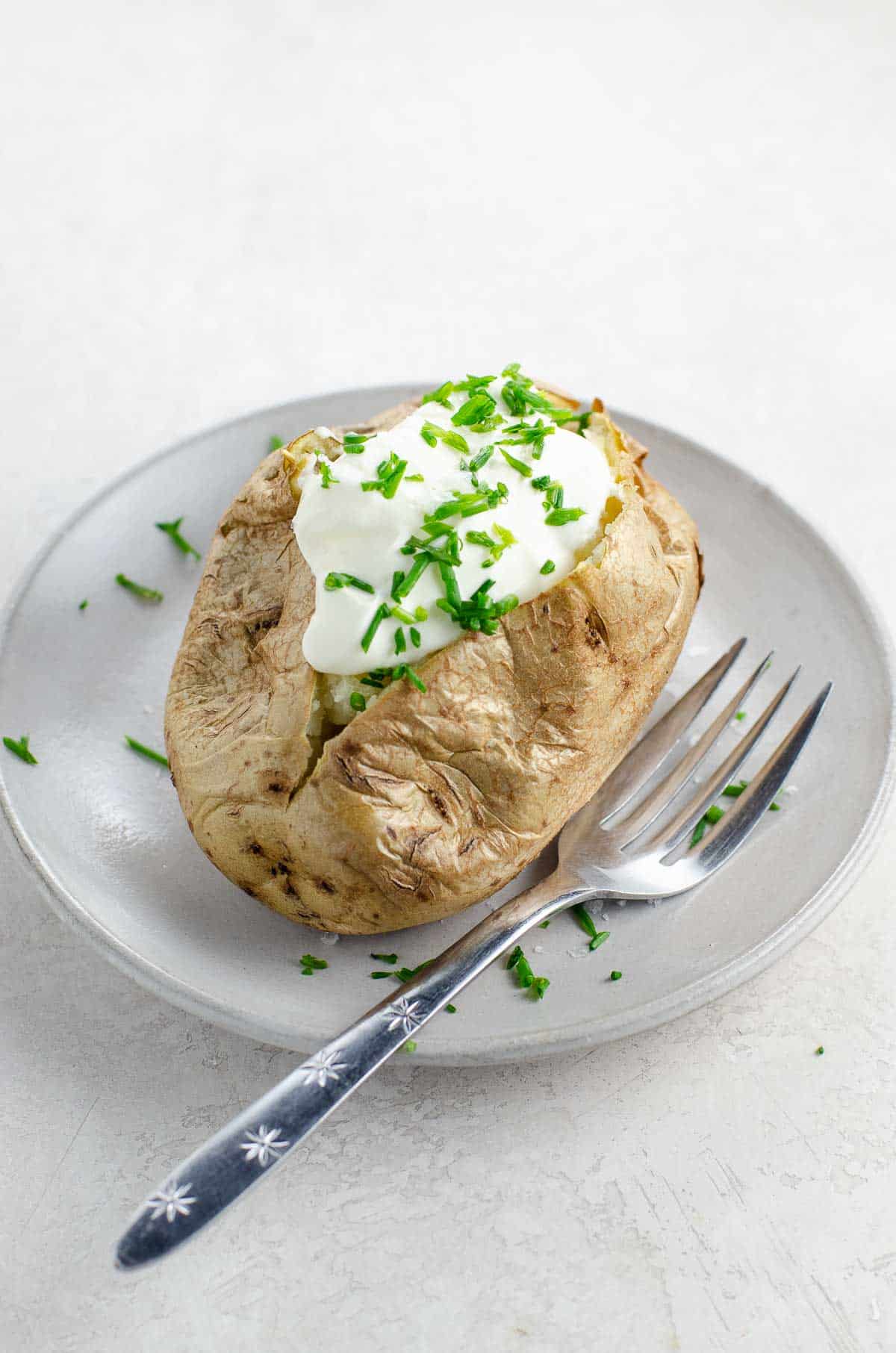 a baked potato with sour cream and chives on a plate with a fork