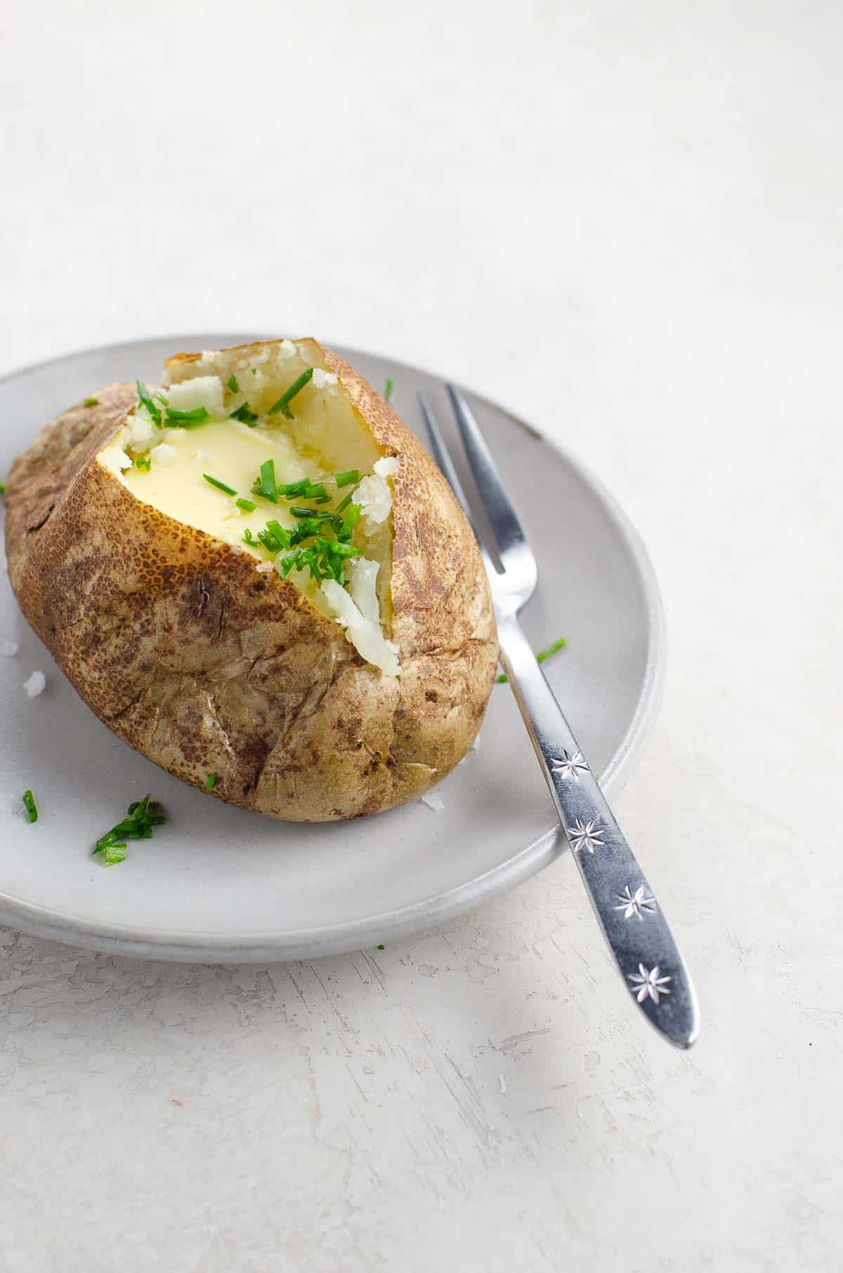 a baked potato with butter and chives on a plate with a fork
