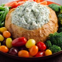 knorr spinach dip in a bread bowl with grape tomatoes, broccoli, baby carrots, and snap peas