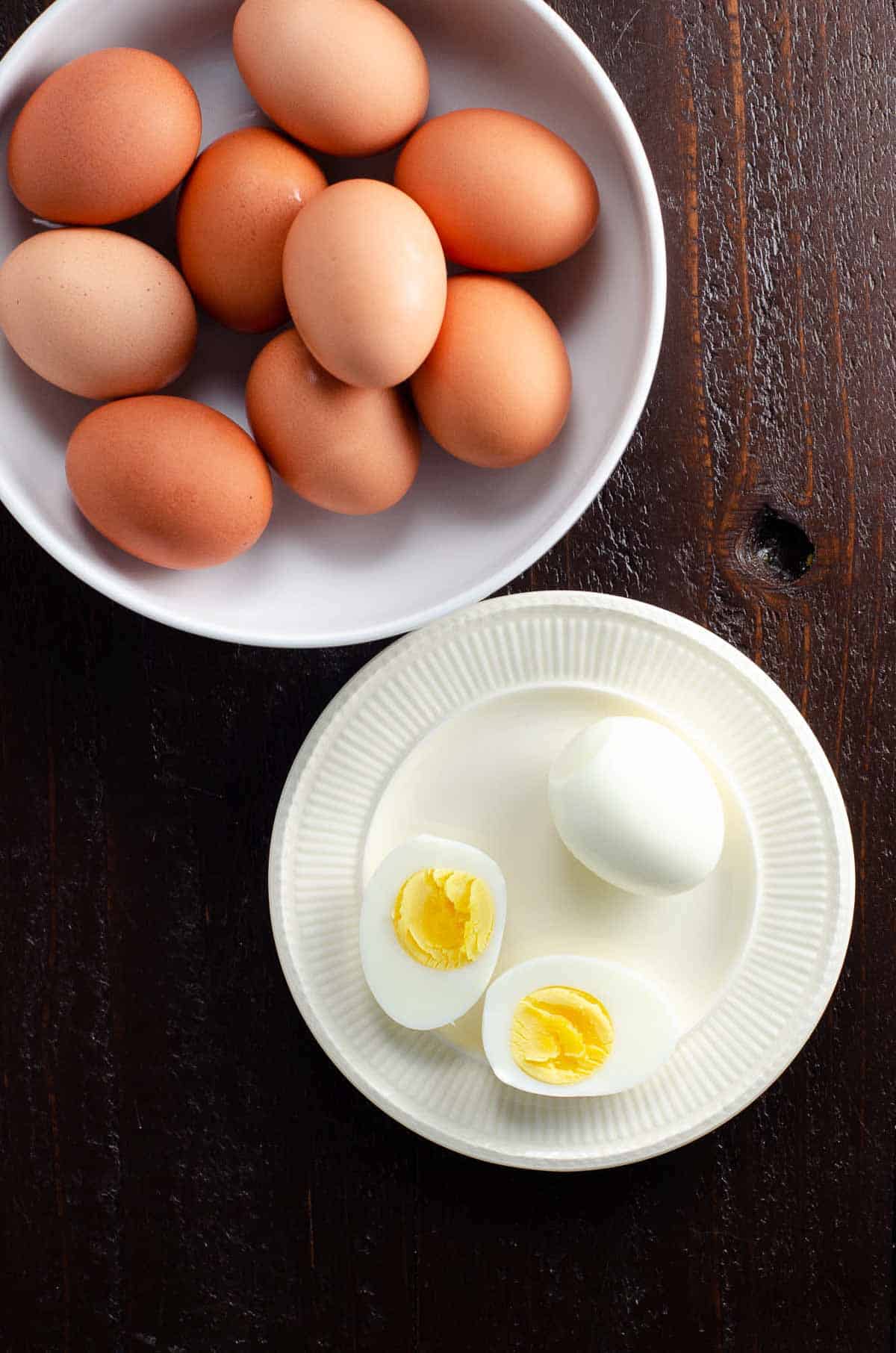 a bowl of hard boiled eggs in their shells, and a small plate with two peeled hard boiled eggs, one cut in half