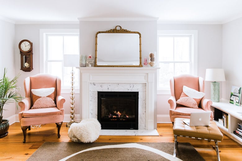 Project January cozy living room with fireplace, pink wingback chairs, laptop, mantle mirror