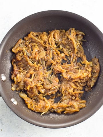 Mahogany-colored caramelized onions in a small frying pan on a white background