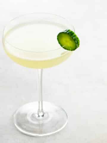 a gin gimlet in a coupe glass garnished with a cucumber slice