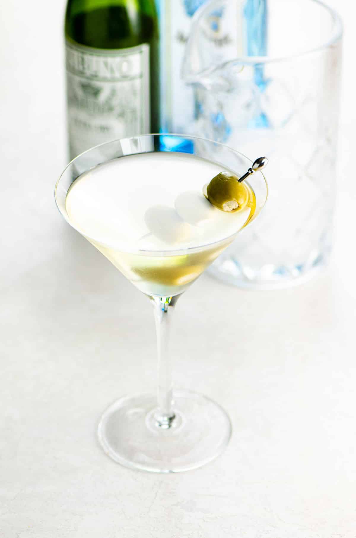 best dirty martini recipe in a glass with bottles of sapphire gin and vermouth in the background