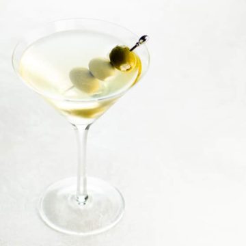 dirty martini with three skewered olives in a martini glass on a light background