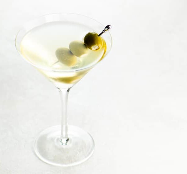 dirty martini with three skewered olives in a martini glass on a light background