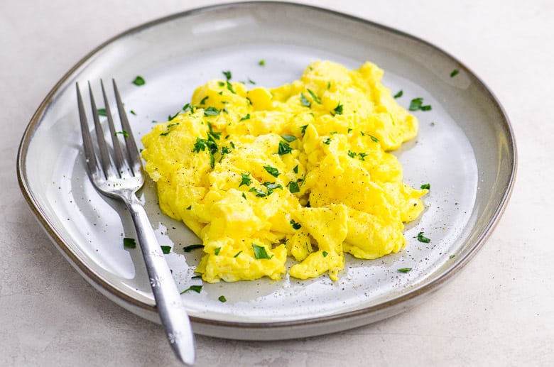 scrambled eggs with parsley and a fork on a grey plate on a light background