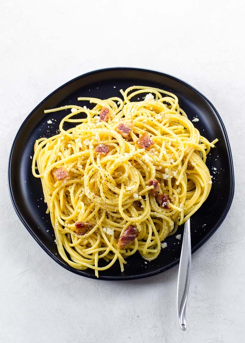 spaghetti carbonara on a black plate with a fork on a light background 