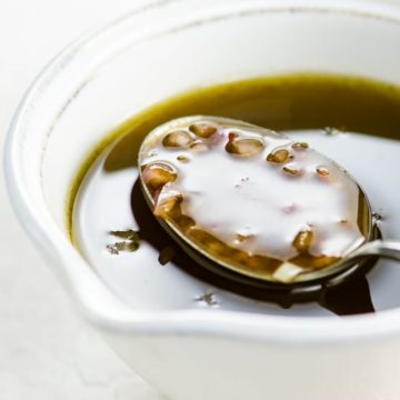 a spoonful of balsamic vinaigrette salad dressing being lifted from a white cup on a white background