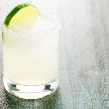 margarita in a rocks glass garnished with a slice of lime on a blue wood background