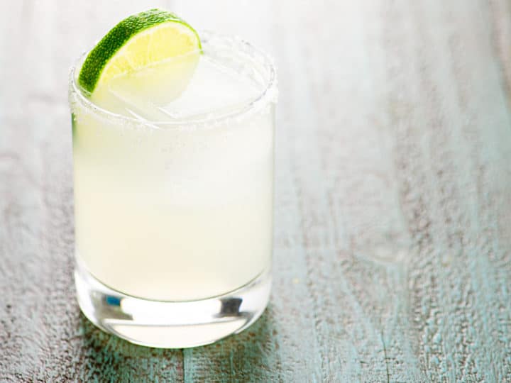 margarita in a rocks glass garnished with a slice of lime on a blue wood background