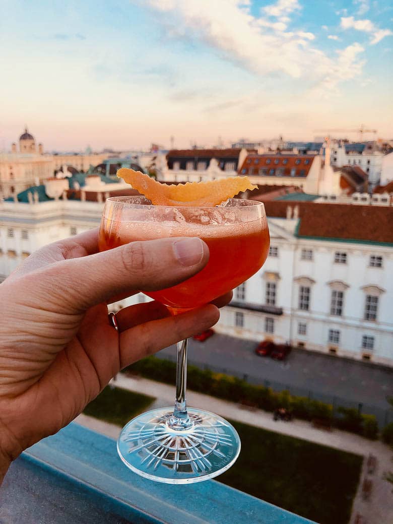 holding a cocktail on a roof deck overlooking the museum quarter of vienna, austria