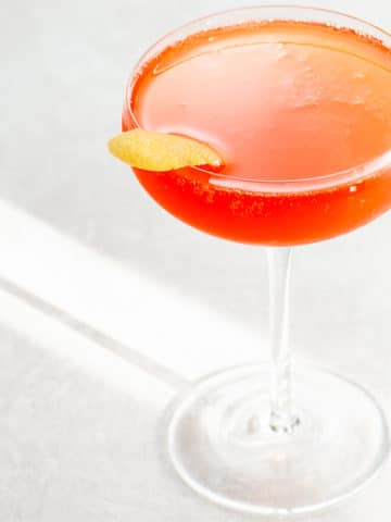 an aperol cocktail in a coupe glass garnished with a grapefruit twist on a light background