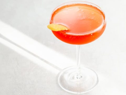an aperol cocktail in a coupe glass garnished with a grapefruit twist on a light background