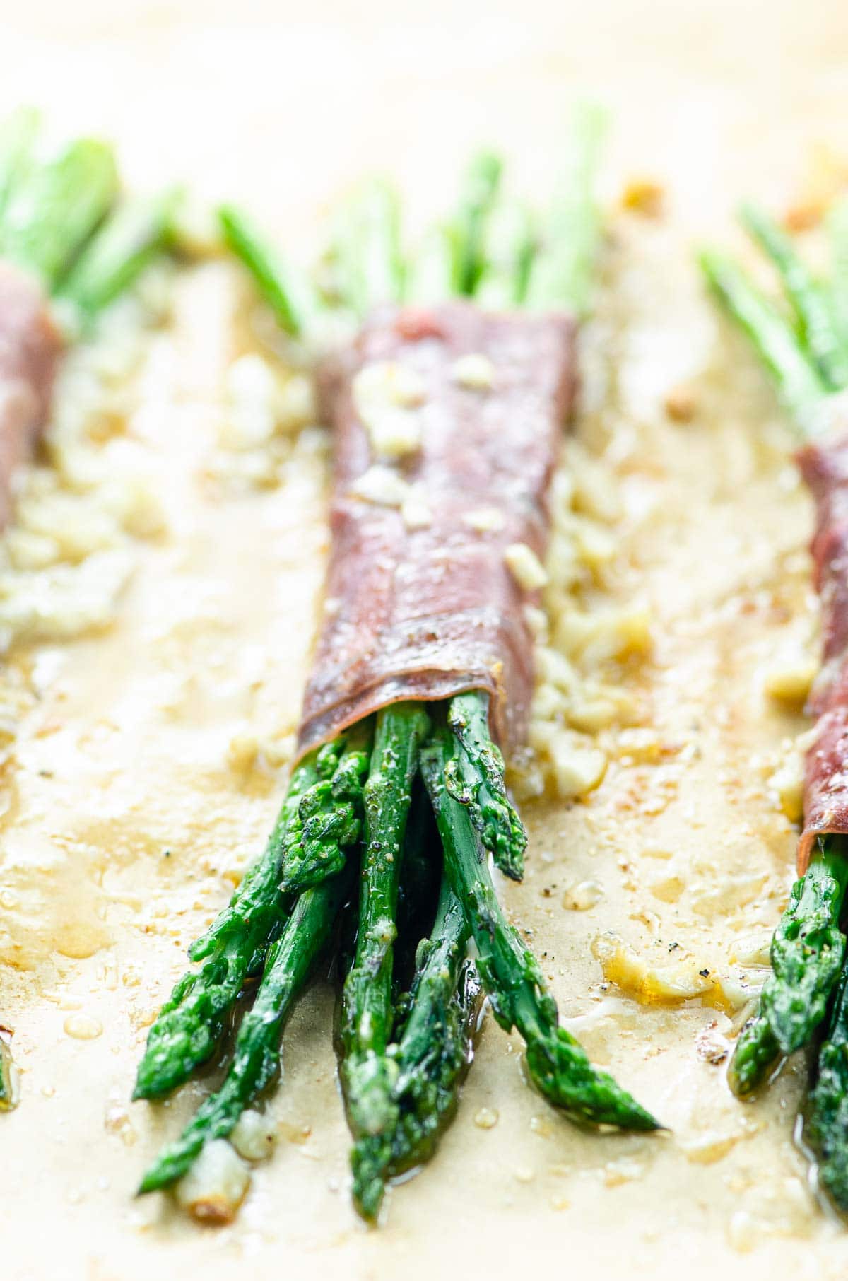 asparagus bundles wrapped with prosciutto on a sheet pan