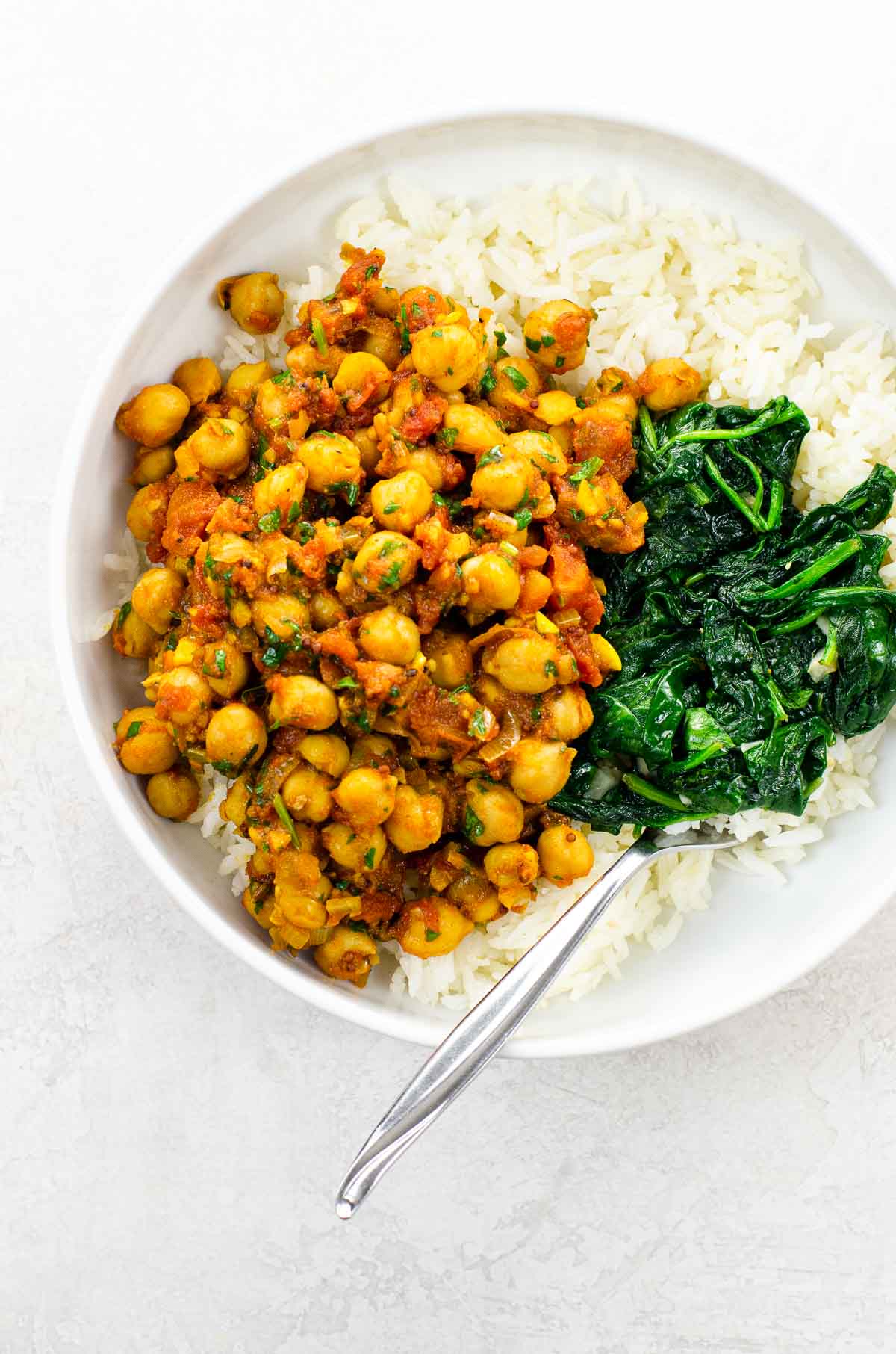 Vegan Chickpea Curry (Chana Masala) in a white bowl with spinach and rice