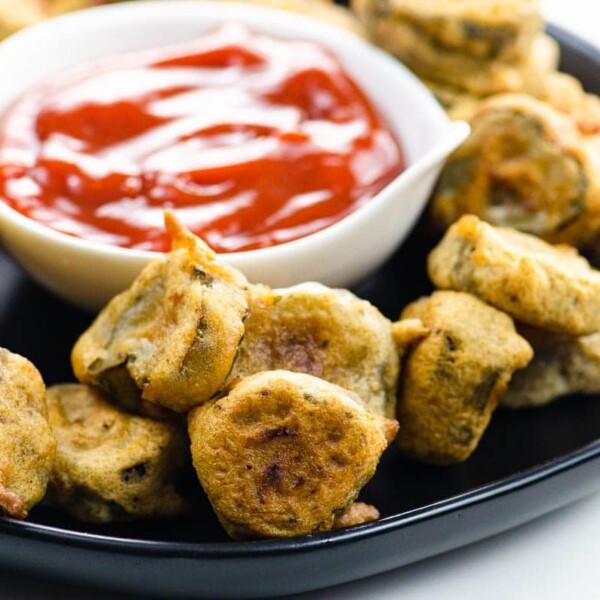 Vegan fried pickles and spicy ketchup on a black plate