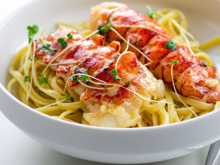 butter poached lobster tails over linguine in a bowl