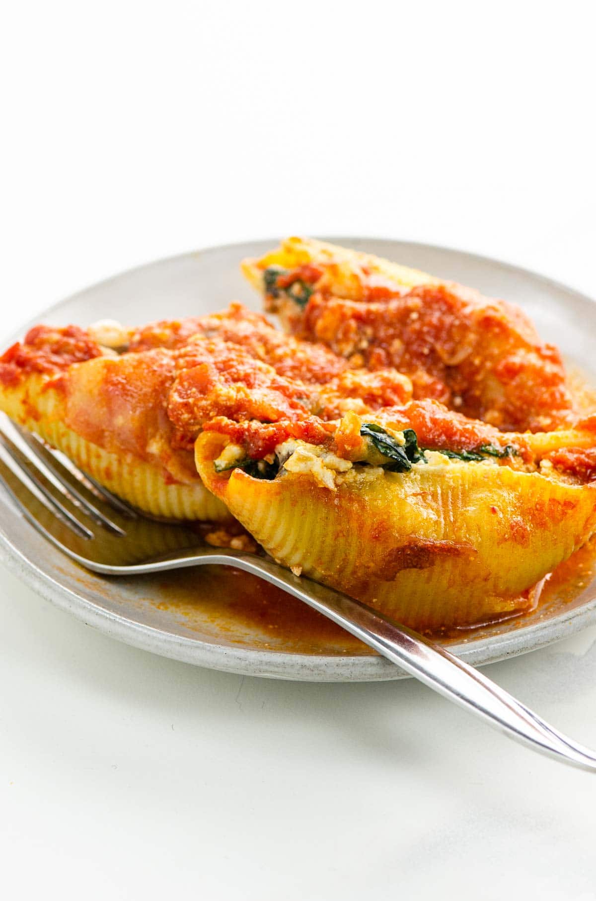 three stuffed pasta shells on a plate with a fork