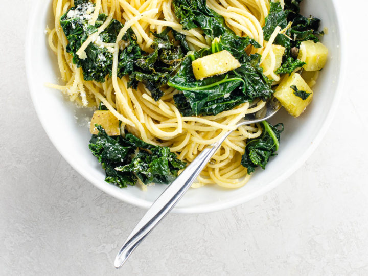 creamy kale pasta with potatoes, lemon, and capers in a white bowl