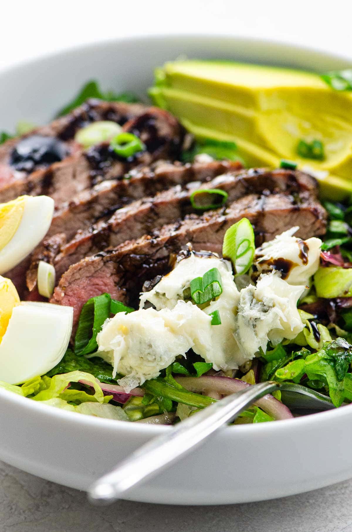 flank steak salad with blue cheese and avocado in a white bowl