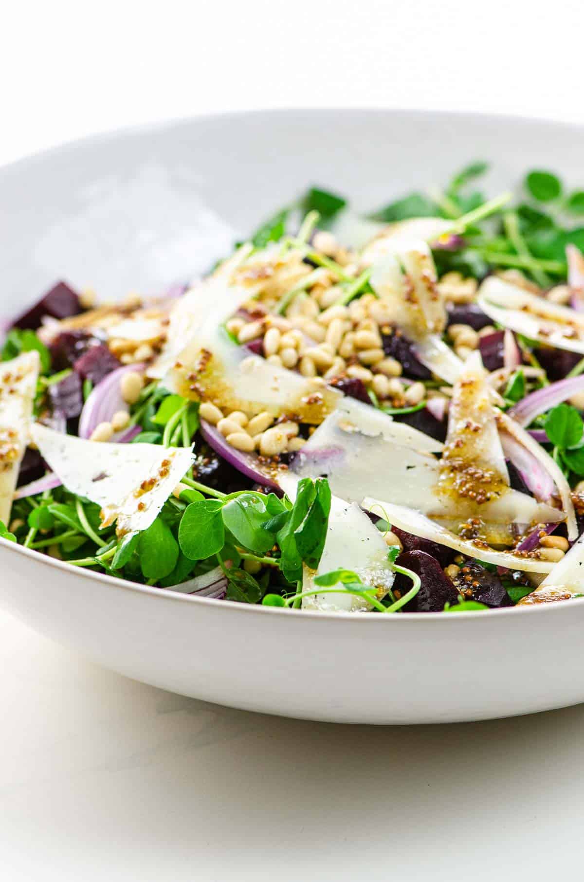 pea shoot salad with manchego, pine nuts, beets, and red onion in a white bowl